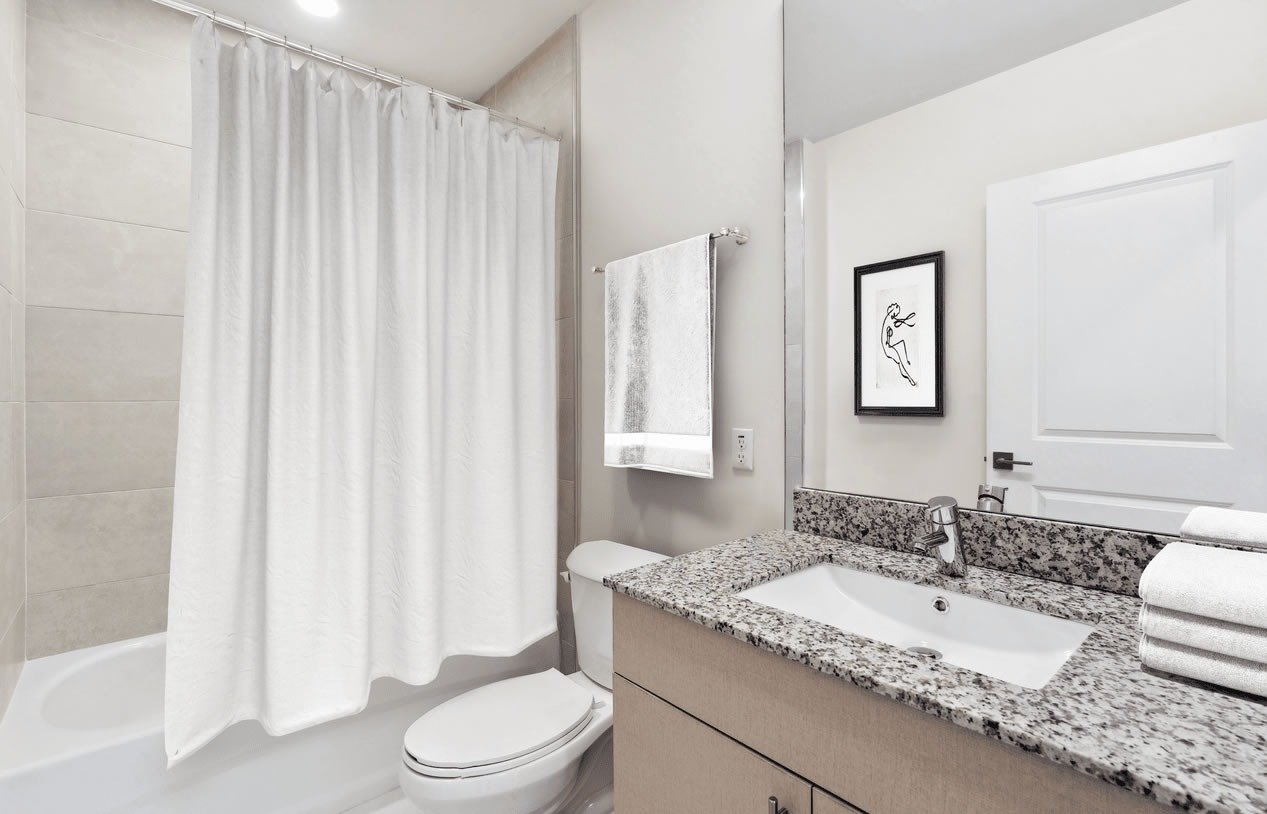 Bathroom with a granite vanity, inset sink, and white tub behind a shower curtain.