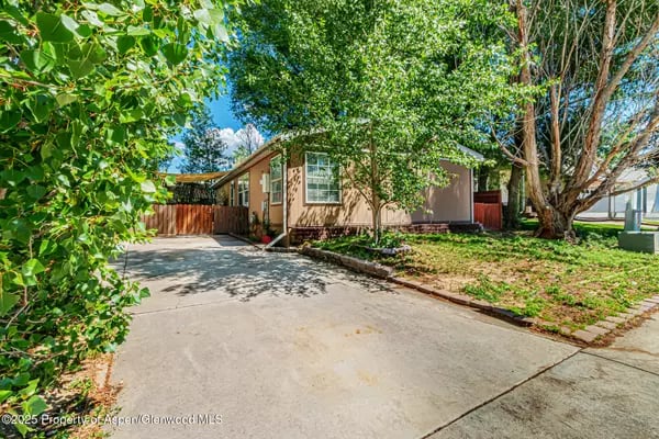 Single-story home shaded by mature trees, with a wide concrete driveway and fenced yard.