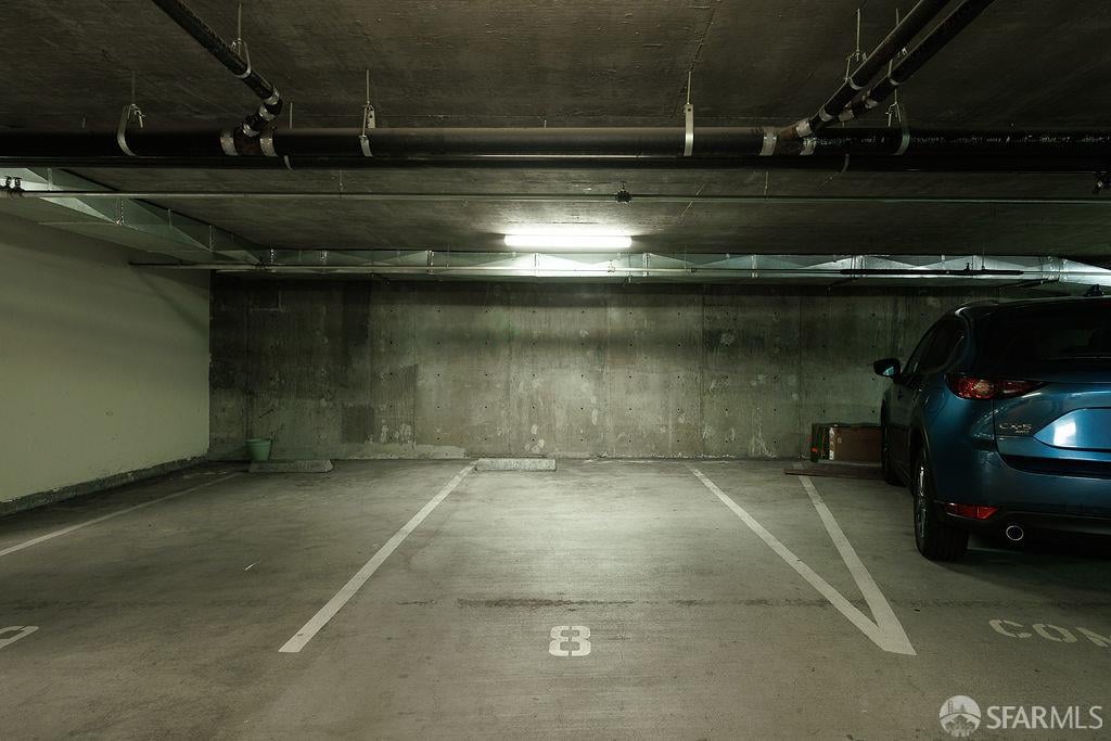 Concrete parking garage with numbered stalls, overhead pipes, and a blue SUV.