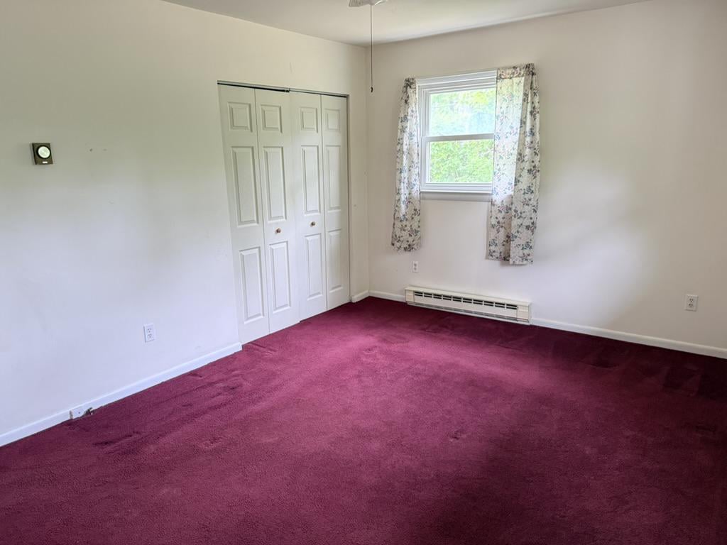 Empty bedroom with burgundy carpet, a double-door closet, and a window with floral curtains.