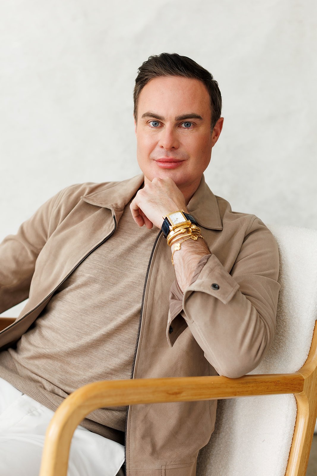 Michael Sweeney seated in a chair, wearing a taupe jacket and wristwatch.