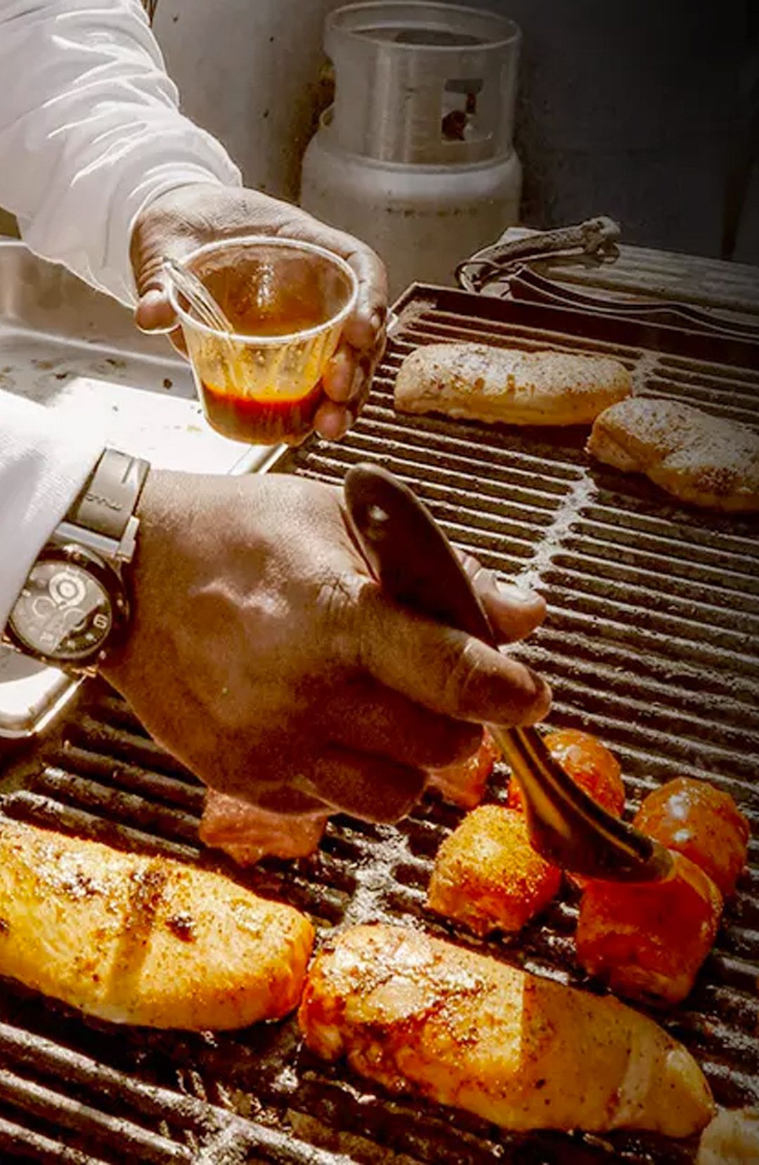 A cook brushes sauce onto meat on a barbecue grill.