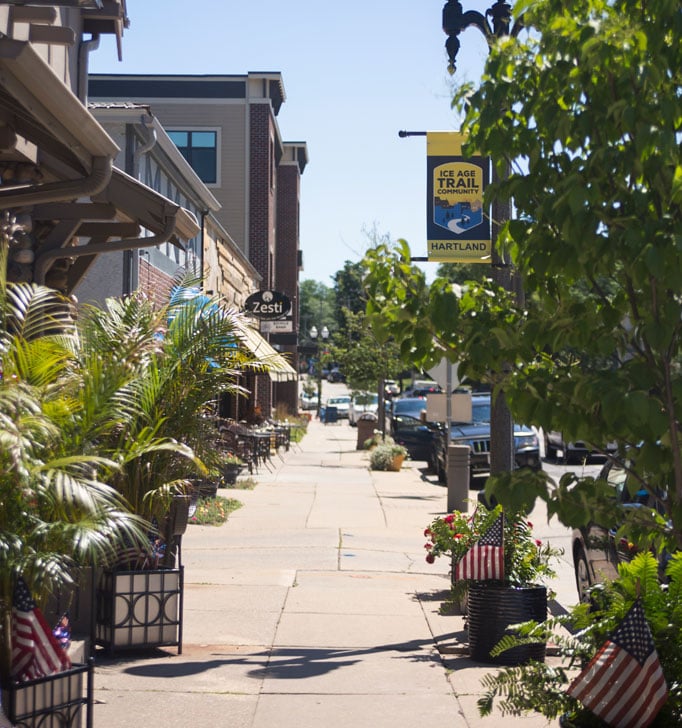 Sidewalk in downtown Hartland with shops, plants, and American flags