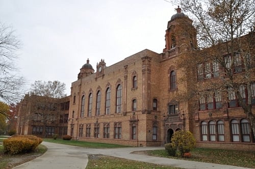 Historic brick school building with arched windows, a prominent tower, and a curved walkway.