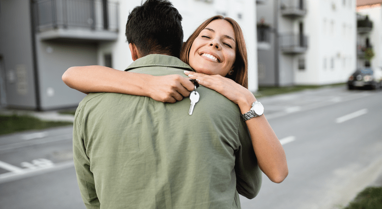 A man and woman embrace affectionately in front of a charming house, showcasing warmth and connection.