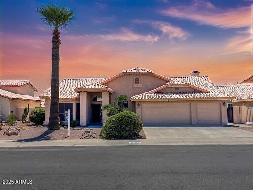 Stucco home with a tiled roof, two-car garage, and palm tree beneath a colorful sunset sky.