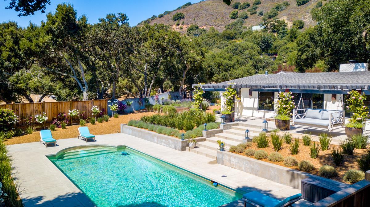 Backyard pool and stone patio with lounge chairs beside a single-story home.