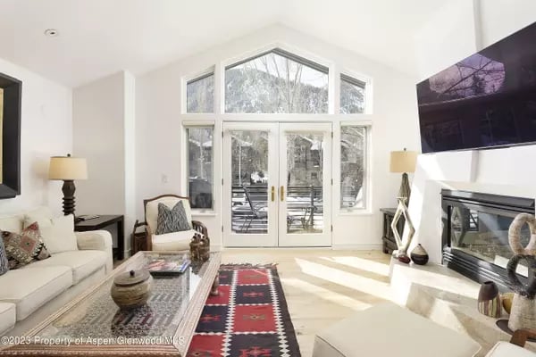 Bright living room with vaulted ceiling, arched window, glass doors, and fireplace.