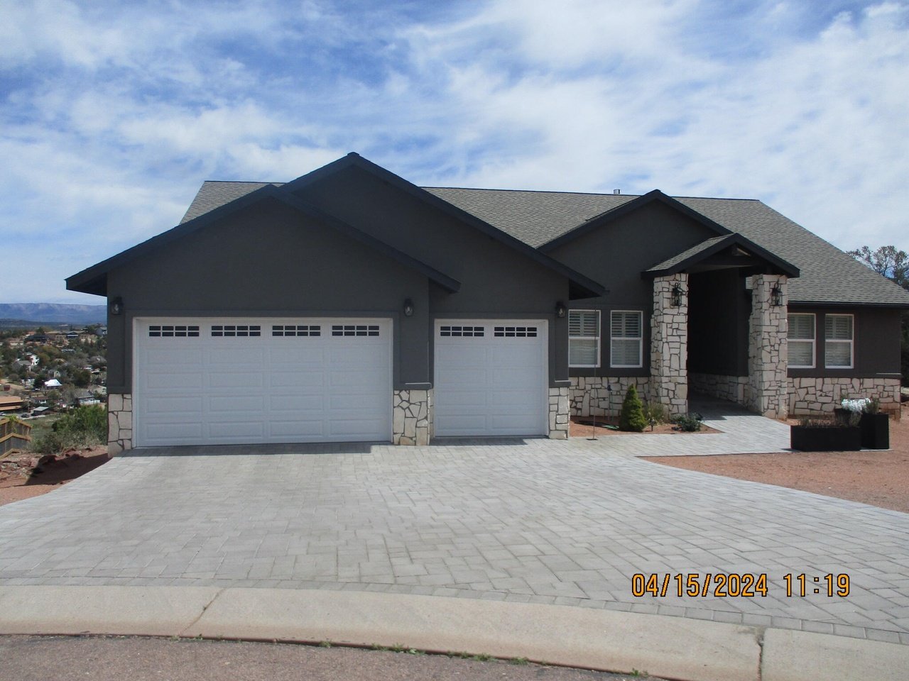 Dark gray house with stone accents, two garage doors, and a broad paved driveway.