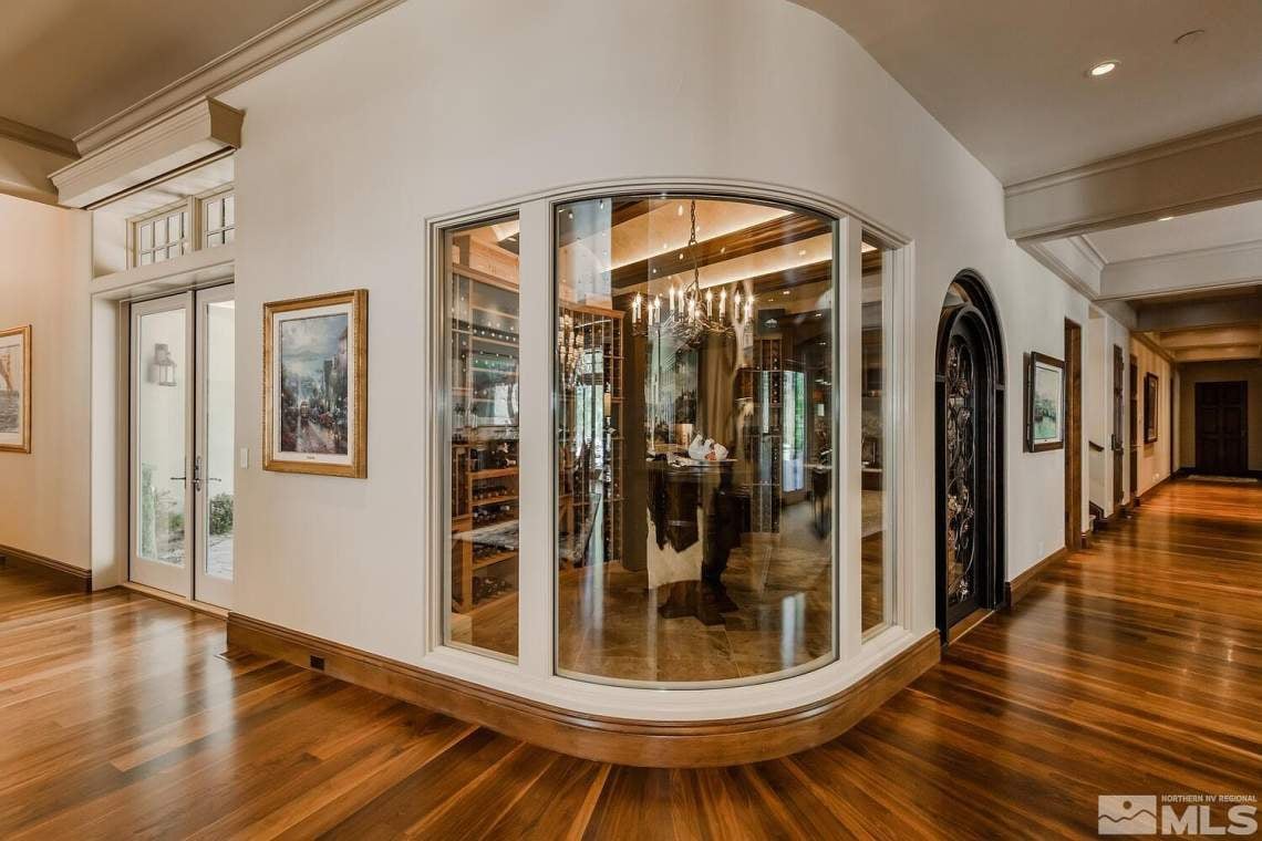 Glass-enclosed wine cellar with curved windows and hardwood floors in a luxury home.