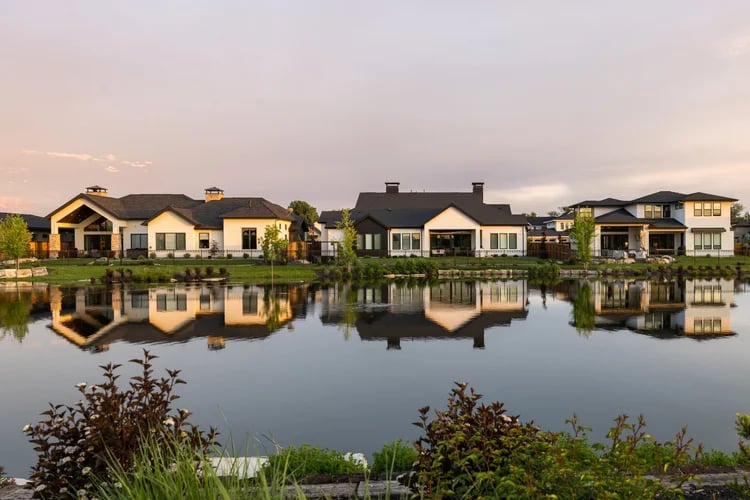 Waterfront homes reflected in a calm pond at sunset.