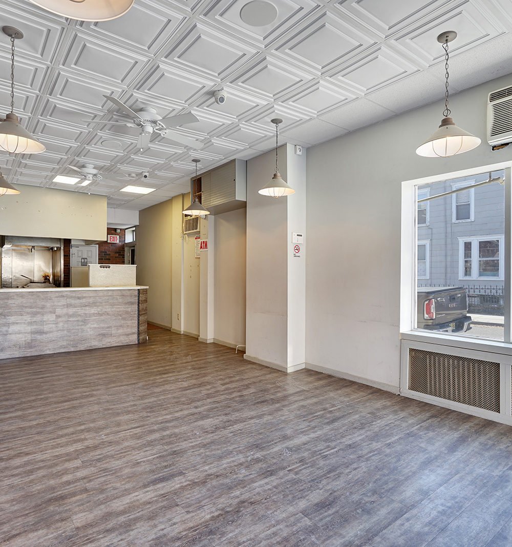 Vacant commercial interior with a service counter, wood-look flooring, and a decorative coffered ceiling.