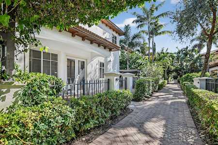 White townhouse beside a brick-paved lane, framed by lush hedges and palm trees.