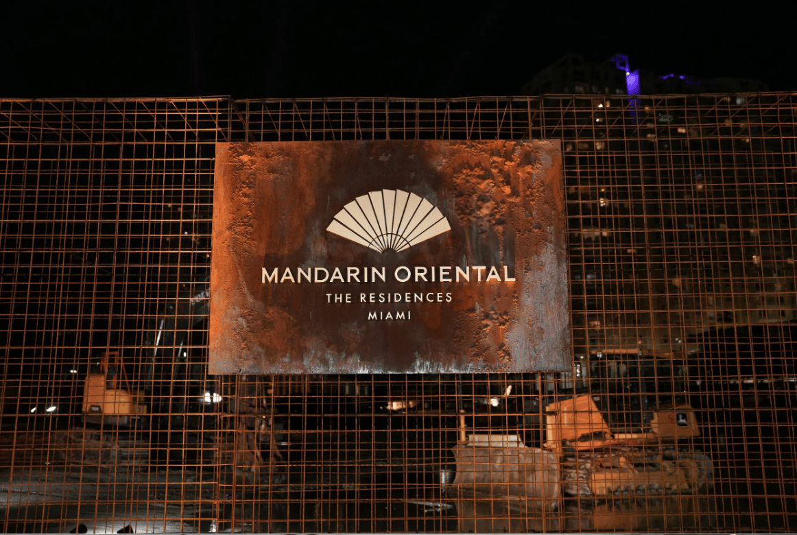 Construction site at night with a Mandarin Oriental Residences Miami sign on the fencing.