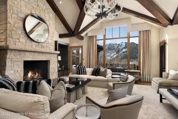 Living room with a stone fireplace, vaulted timber beams, and large windows overlooking snowy mountains.