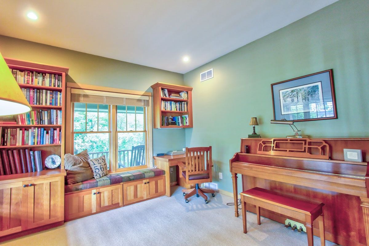 Furnished home office with built-in bookshelves, a window seat, and a wooden piano.