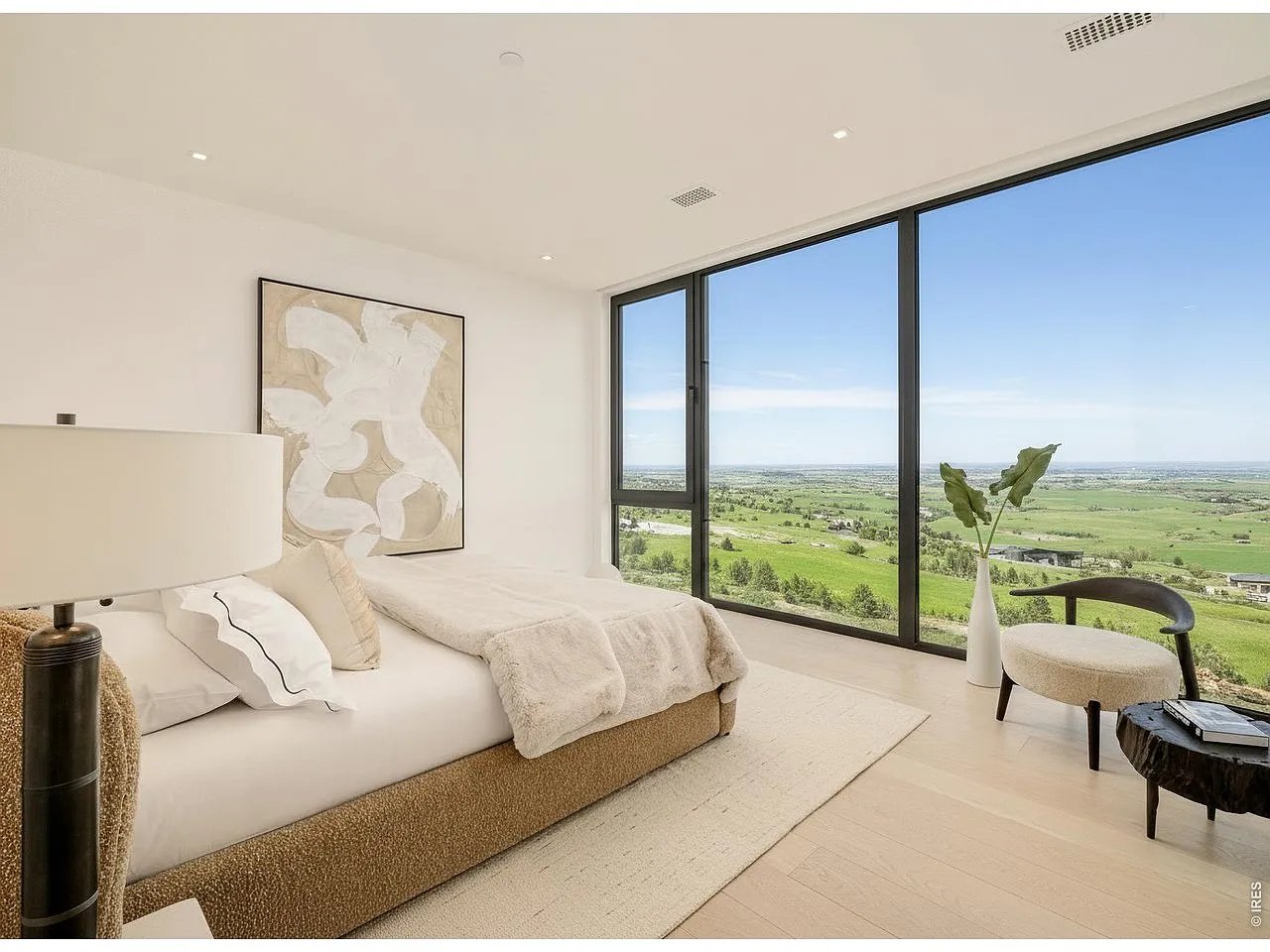 Bedroom with a low upholstered bed and expansive windows overlooking green plains.