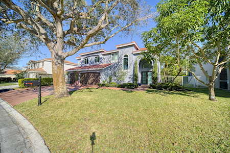 Two-story stucco home with a red tile roof, broad lawn, and mature trees.
