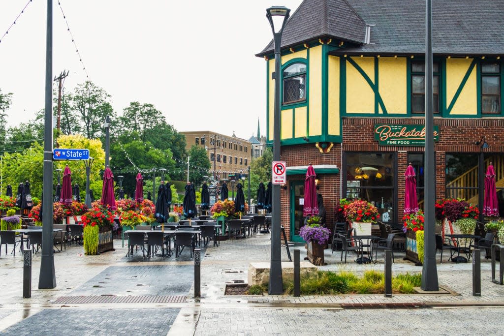 Outdoor dining area and shops in Wauwatosa’s Village district, showing colorful flowers, patio seating, and historic storefronts.