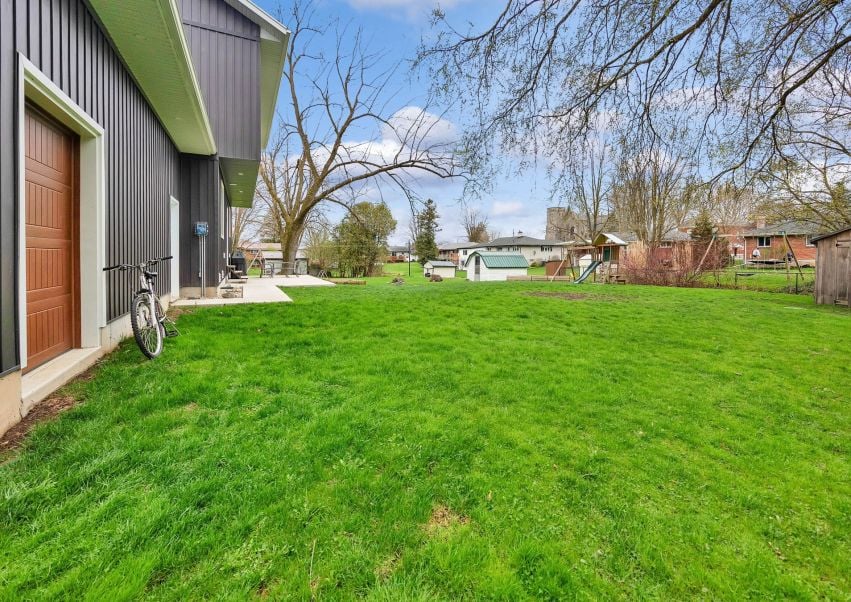 Green backyard beside a modern home, with a bicycle by the wall and a playset in the distance.