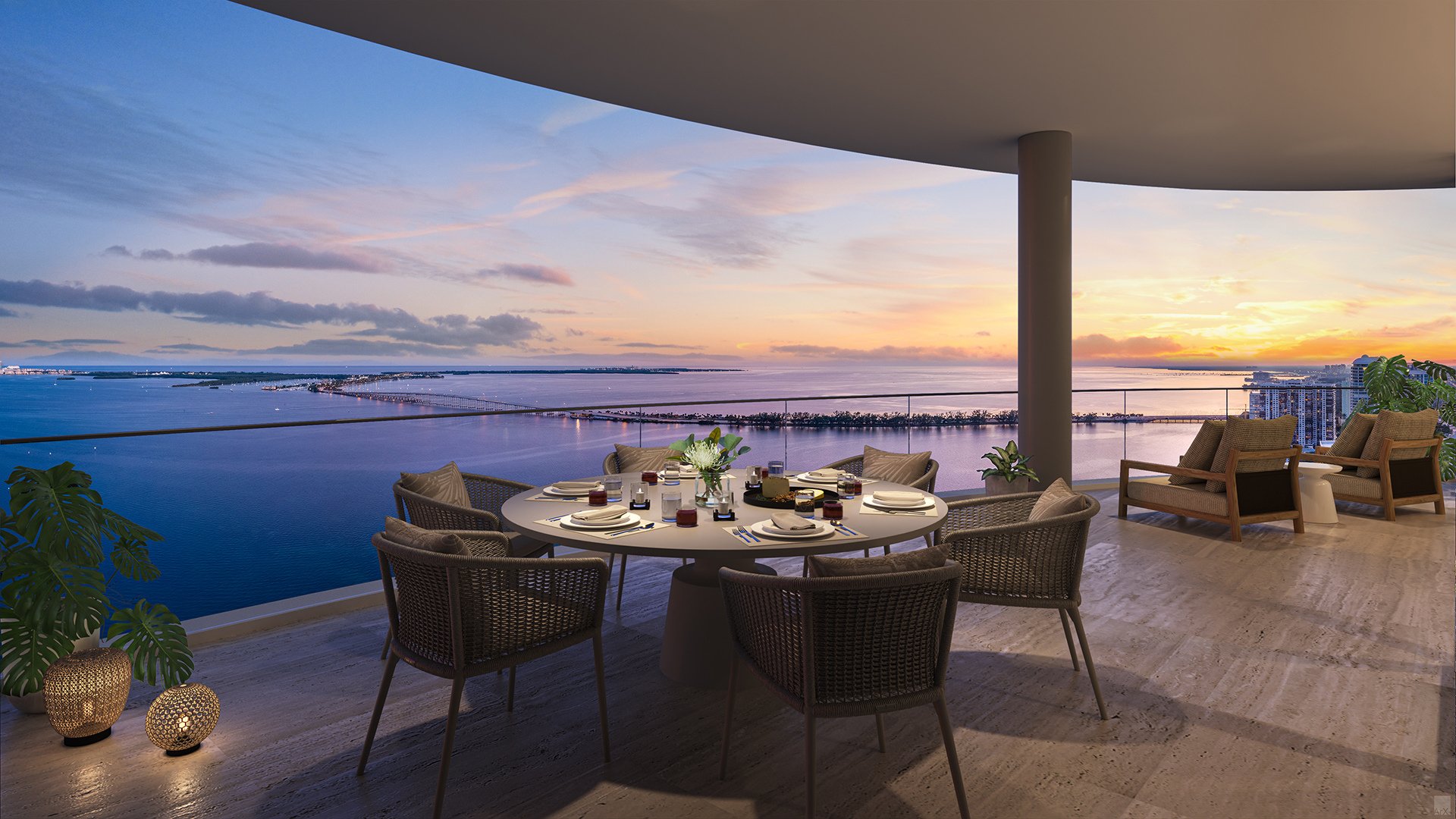 Furnished terrace with outdoor dining and lounge seating overlooking the water at sunset.
