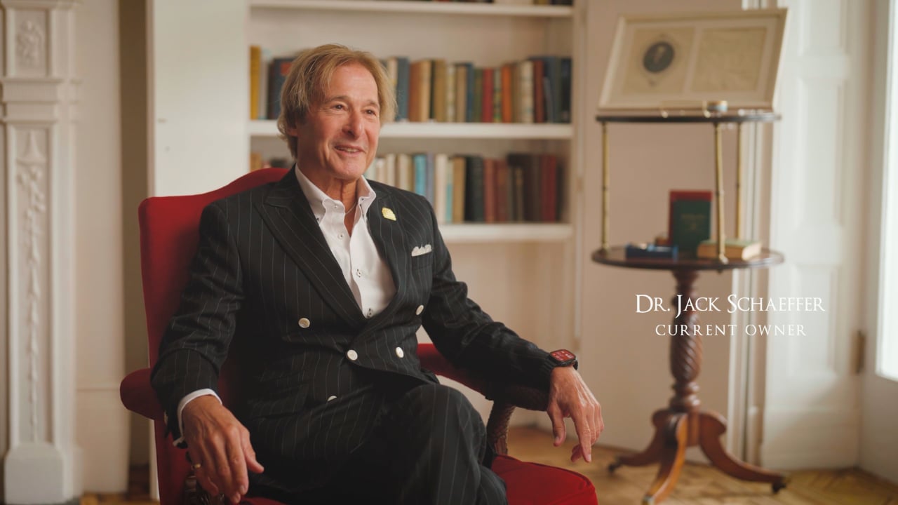 Dr. Jack Schaeffer seated in a red armchair in front of bookshelves.
