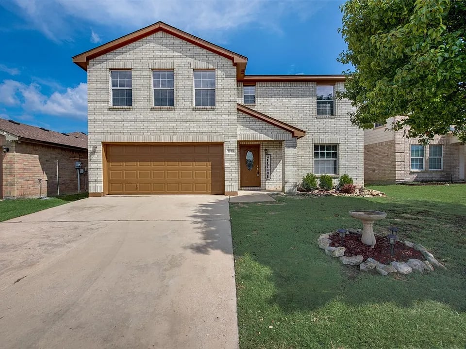 Two-story brick house with a brown double garage, wide driveway, and landscaped front lawn.