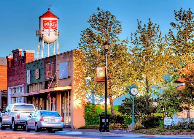 Downtown Frisco street with a brick building, autumn trees, and a water tower marked FRISCO.