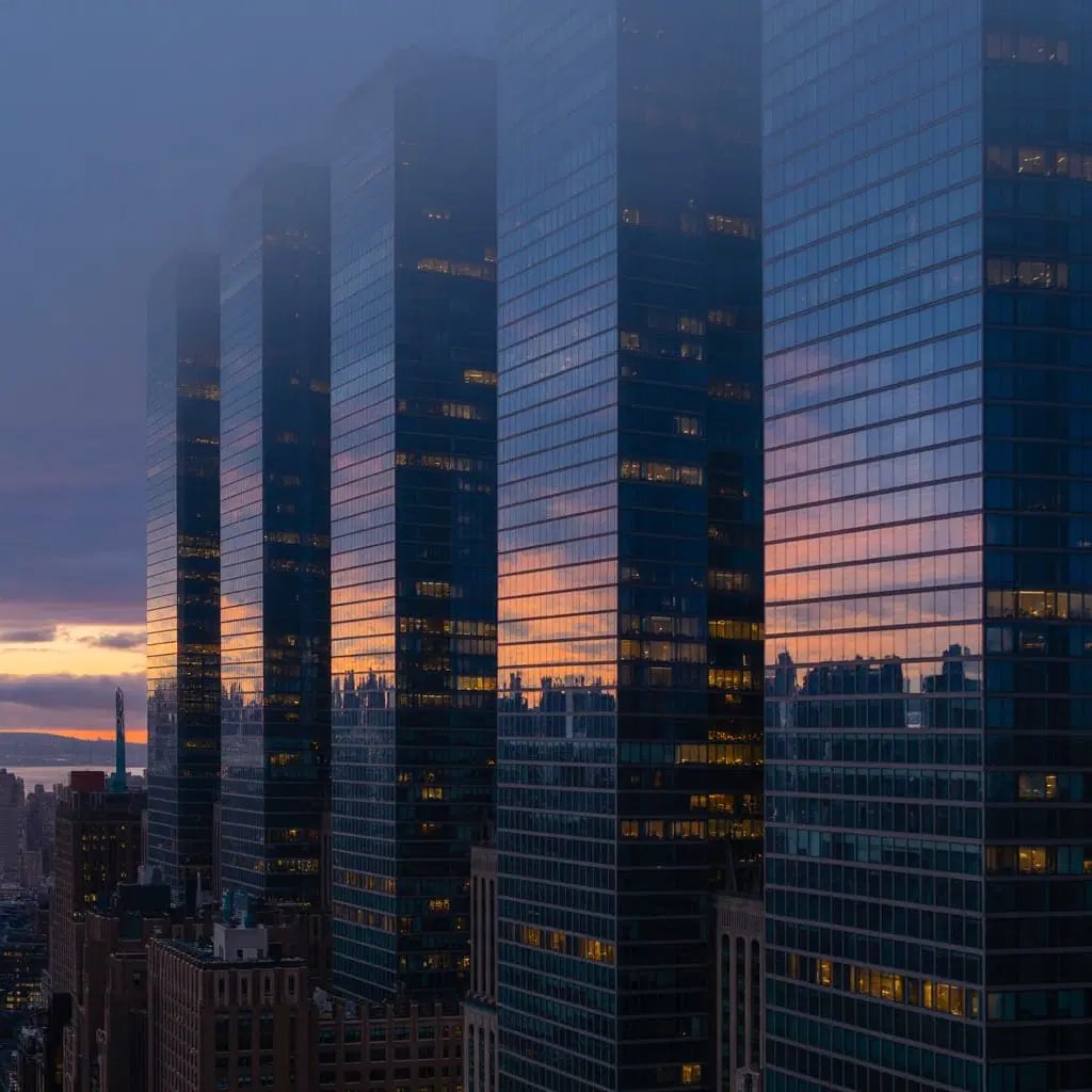 Modern glass skyscrapers in New York City reflecting the sunset sky.