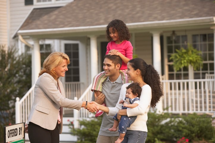 A luxury realtor welcoming a young family to a contemporary estate at sunset, symbolizing a seamless and emotional white-glove relocation transition.