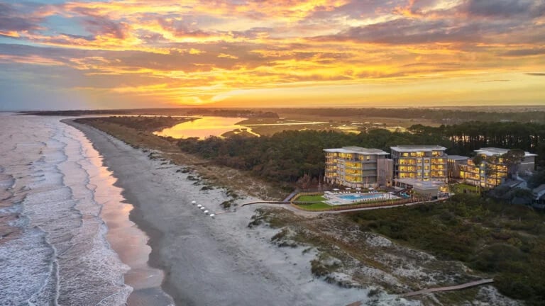 Aerial view of a beachfront residence club with illuminated buildings and pool at sunset.
