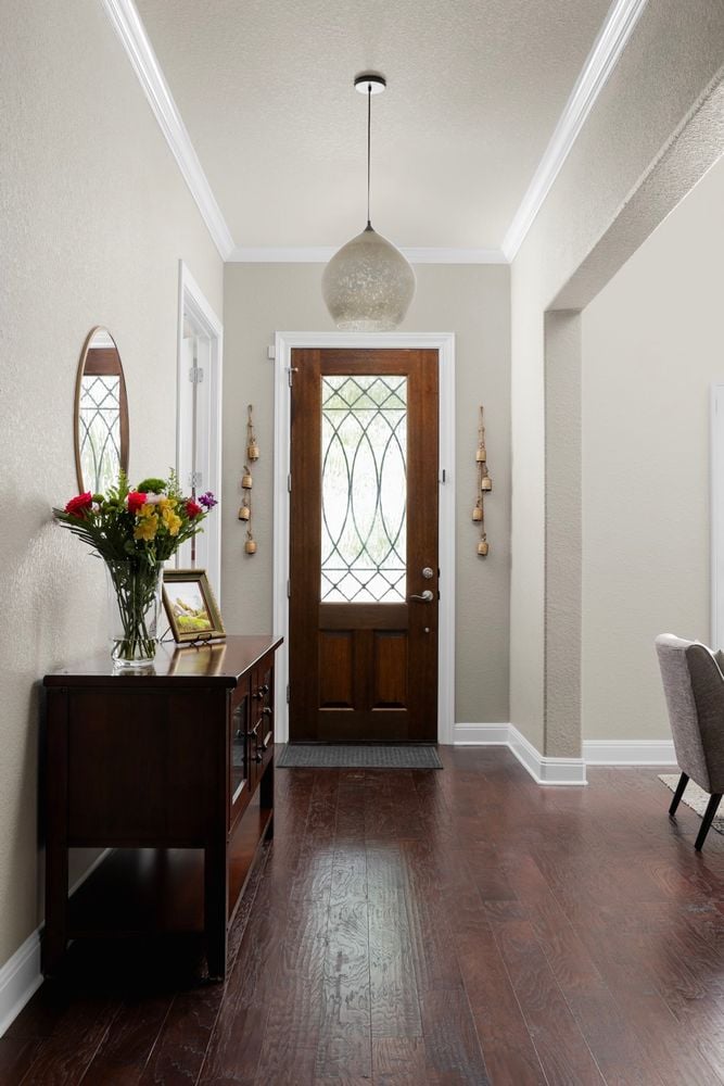 Entry hall with a leaded-glass wood door, hardwood floors, pendant light, and flower-topped console table.