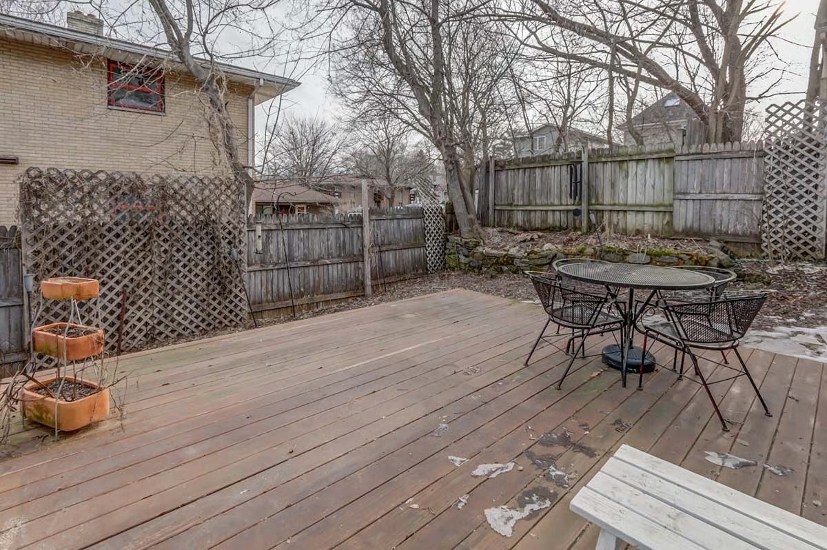 Backyard deck with a metal patio table and chairs, weathered fencing, and leafless trees.