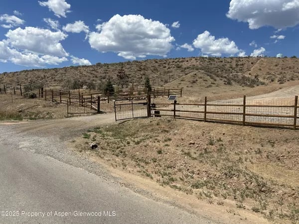 Open Silt parcel with a metal gate and fence beside a gravel road, backed by dry hills.