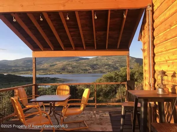 Covered wooden deck with patio seating overlooking a lake and mountain landscape.