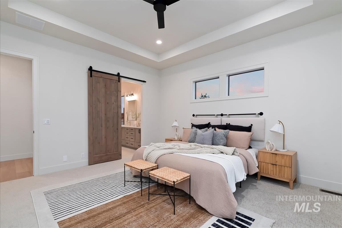 Primary bedroom with king-size bed with blush-colored linens, abstract area rug, and oak barn door leading to the bathroom