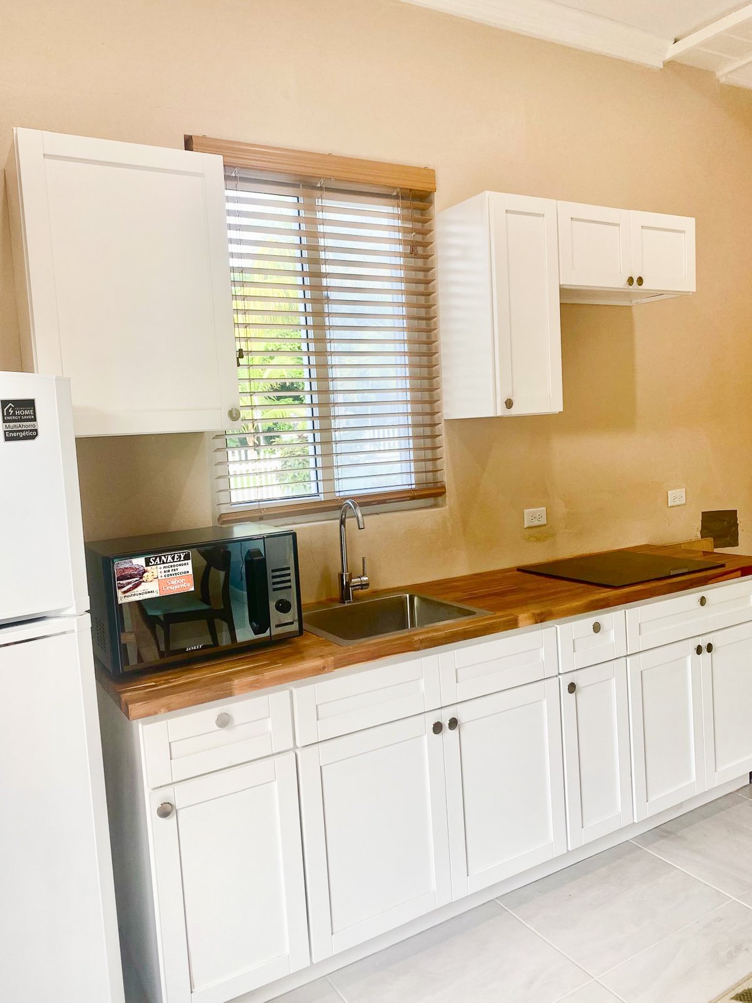 Kitchen with white cabinets, wood countertops, a sink beneath a window, and a black cooktop.