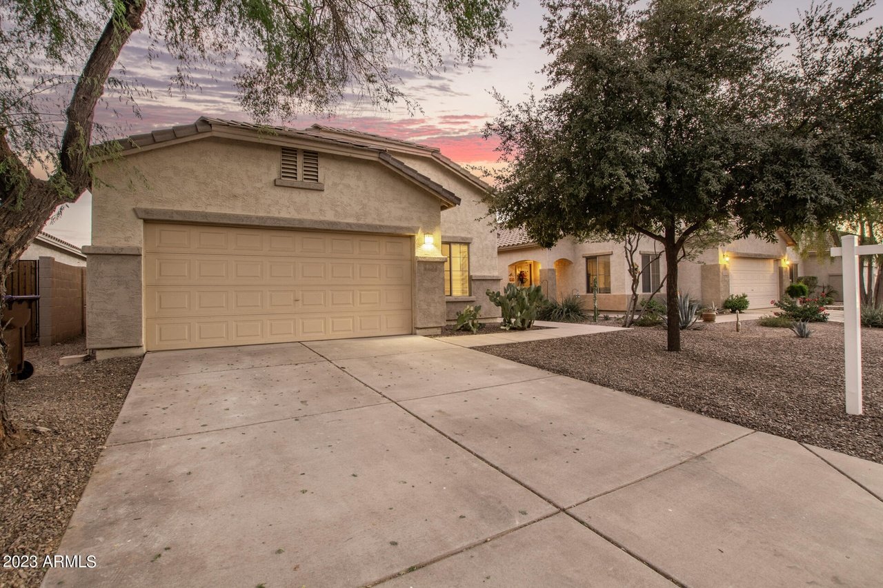 Stucco home with a two-car garage, broad driveway, and desert landscaping at dusk.