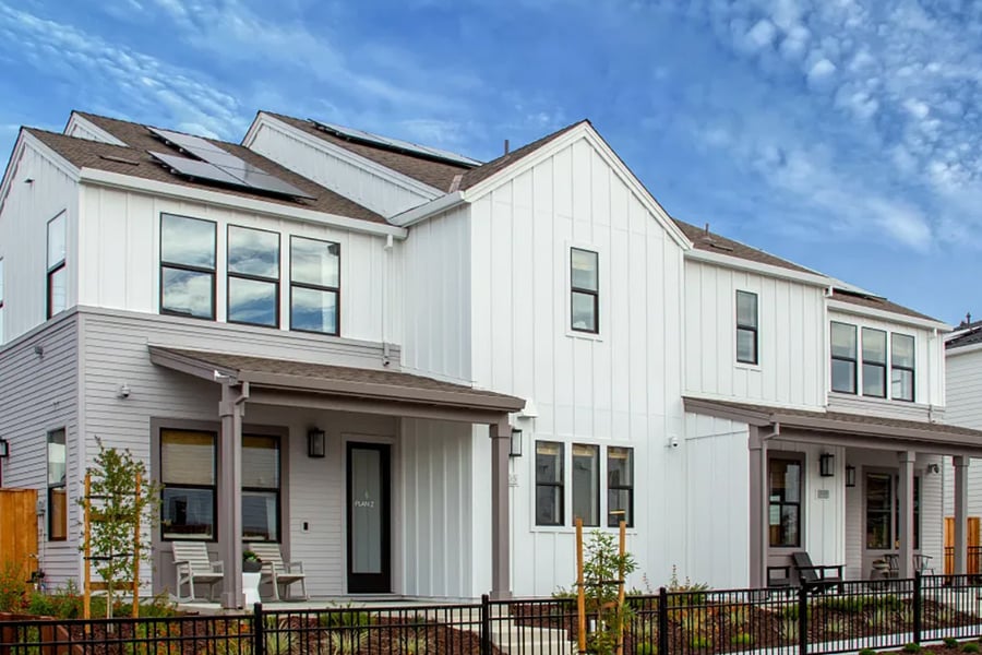 Modern white multi-unit building with solar panels and small fenced patios.