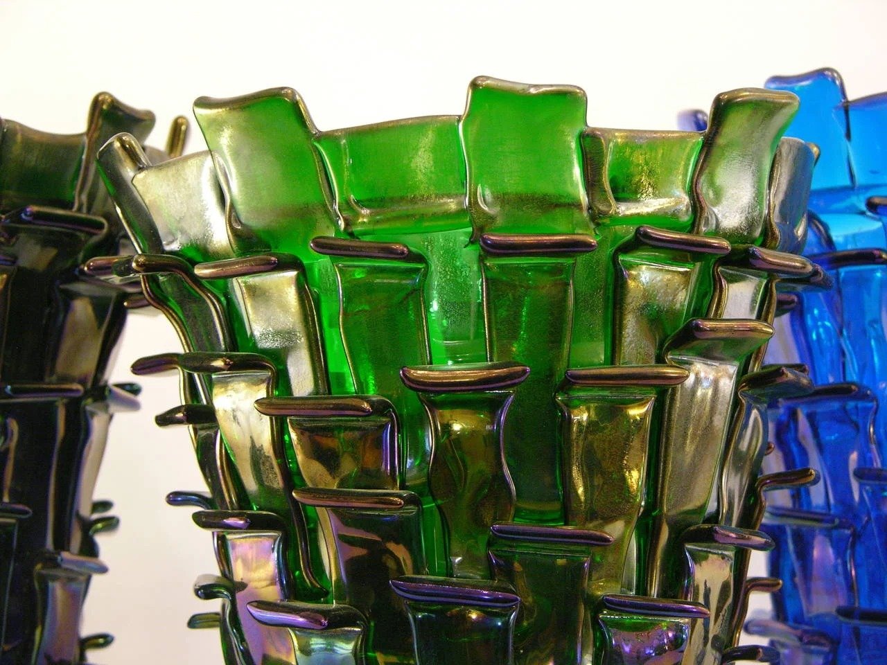 Sculptural arrangement of green, blue, and amber glass pieces with folded forms and dark purple rims.