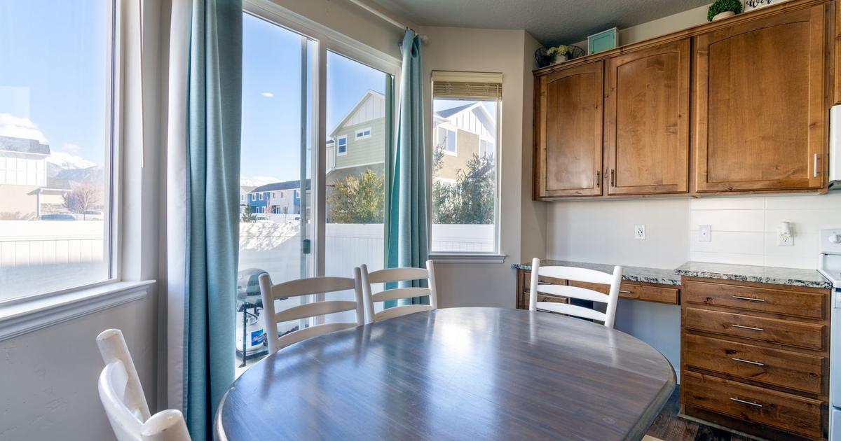 Kitchen dining area with a round table, wood cabinets, and teal curtains.