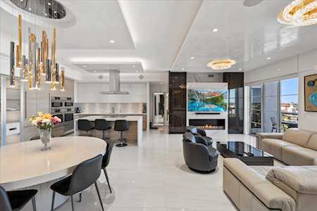 Open-plan living room and kitchen with a white island, fireplace, and expansive windows.