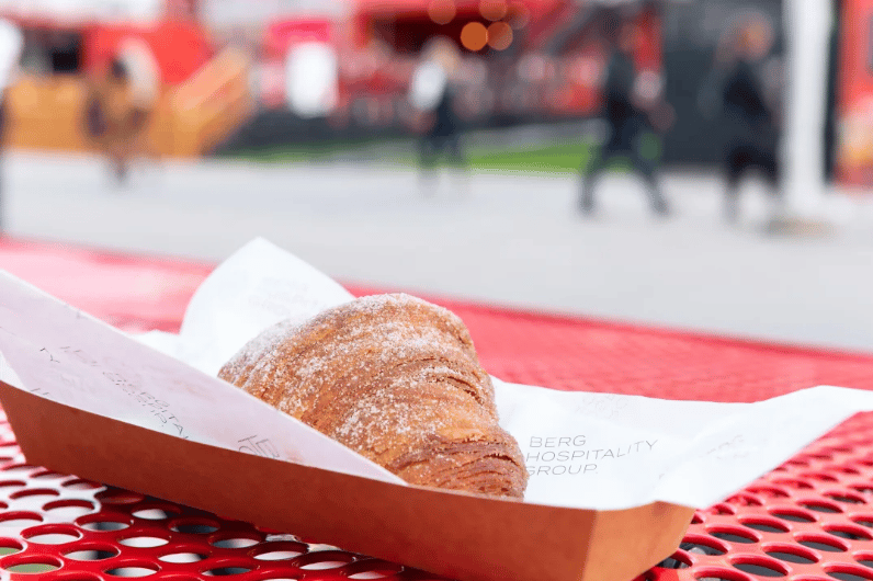 Sugar-dusted flaky pastry in a paper tray on a red perforated table.