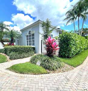 White stucco building with tall windows, tropical landscaping, and a curved brick-paver walkway.