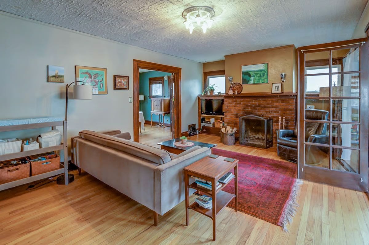 Living room with a brick fireplace, red patterned rug, and ornate pressed-tin ceiling.