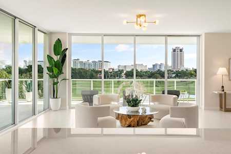 Modern living room with floor-to-ceiling windows overlooking greenery and city buildings.