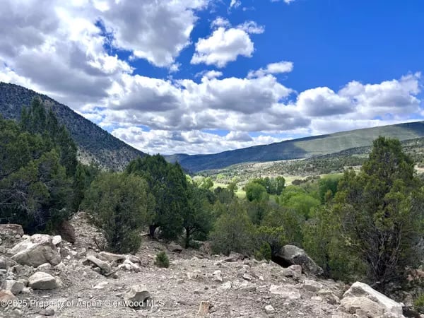 Green Gypsum valley framed by wooded hills, with a rocky slope in the foreground.