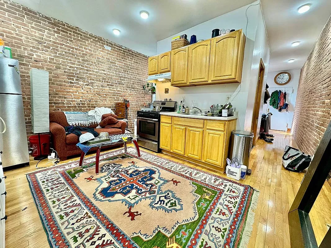 Open-plan kitchen and living area with exposed brick walls, wood cabinets, and a large patterned rug.