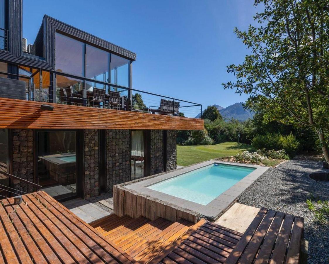 Modern glass-and-stone house with a wooden deck, swimming pool, and mountain views.