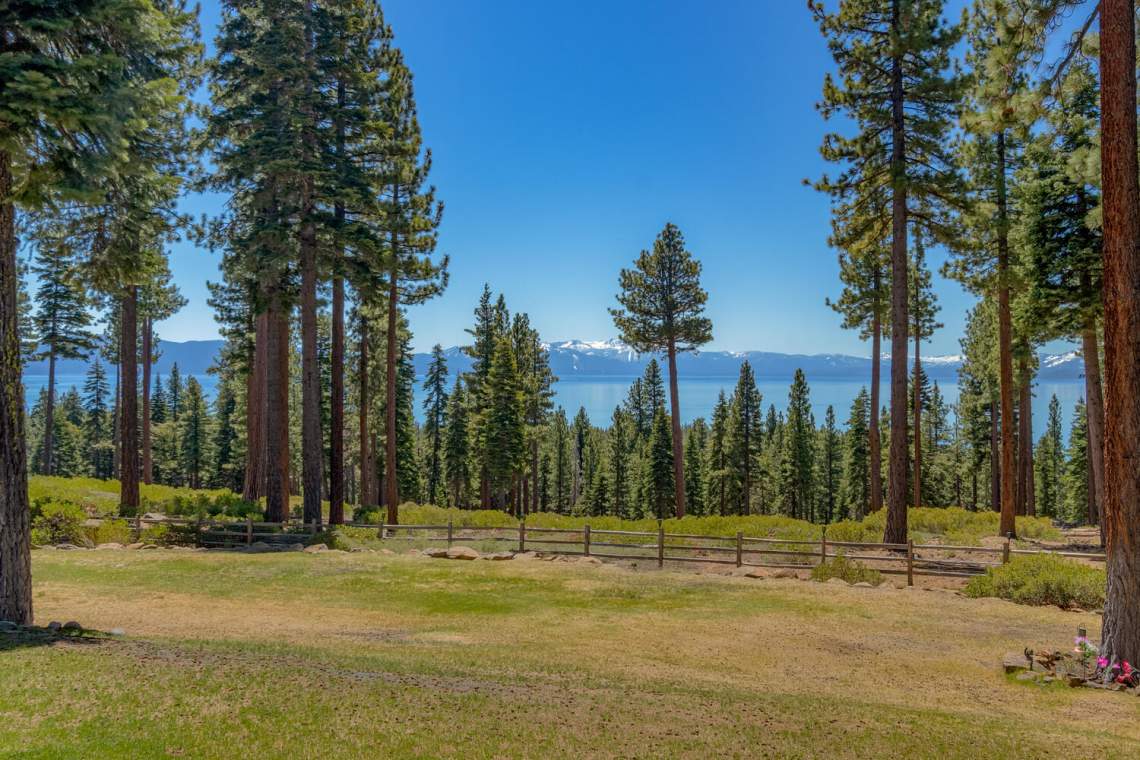 Grassy Tahoe City estate grounds framed by pines, overlooking Lake Tahoe and snow-capped mountains.
